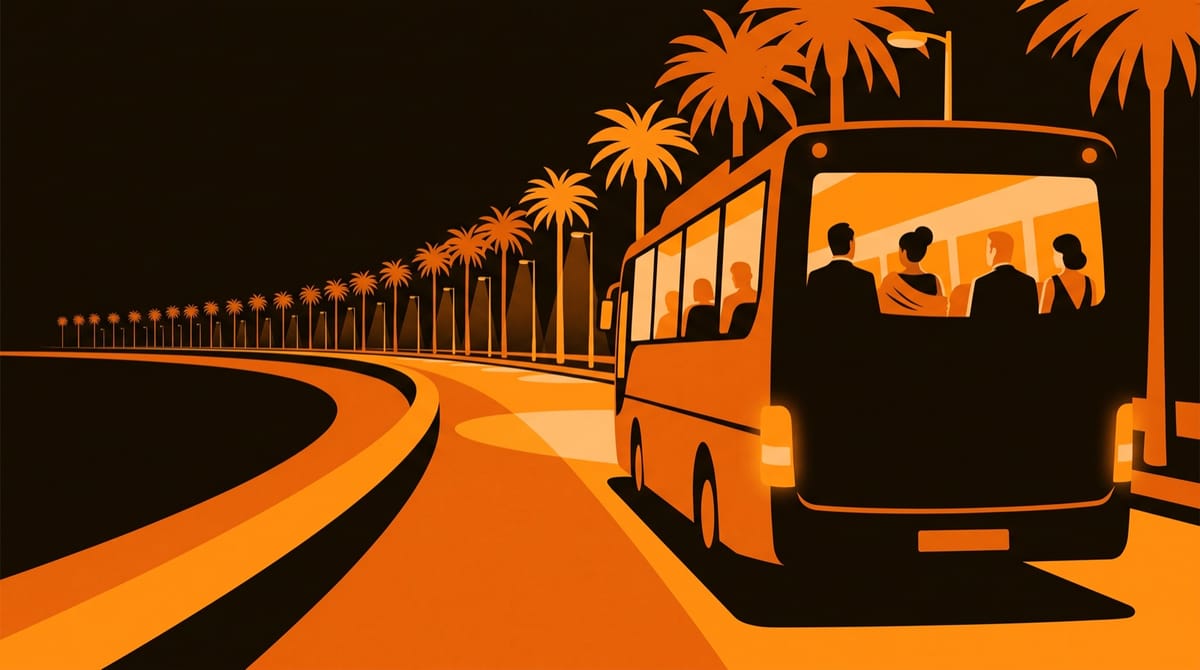 A festival shuttle bus pulling away along a waterfront promenade at night, seen from the pavement behind it.